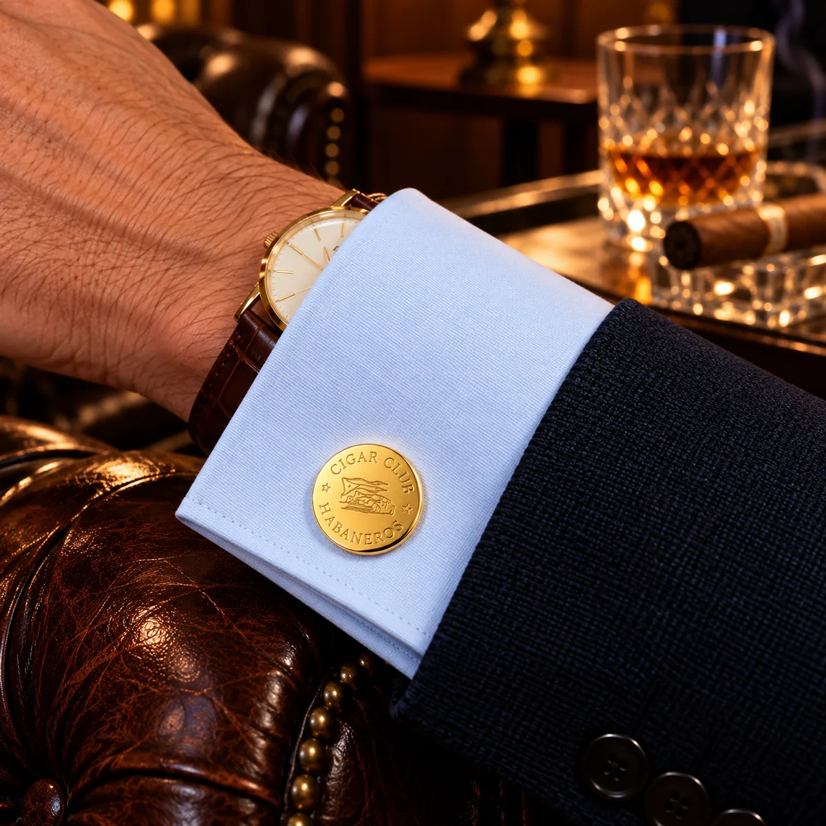 Man in clubfauteuil draagt ronde goudkleurige manchetknoop met het logo van Cigar Club Habaneros
